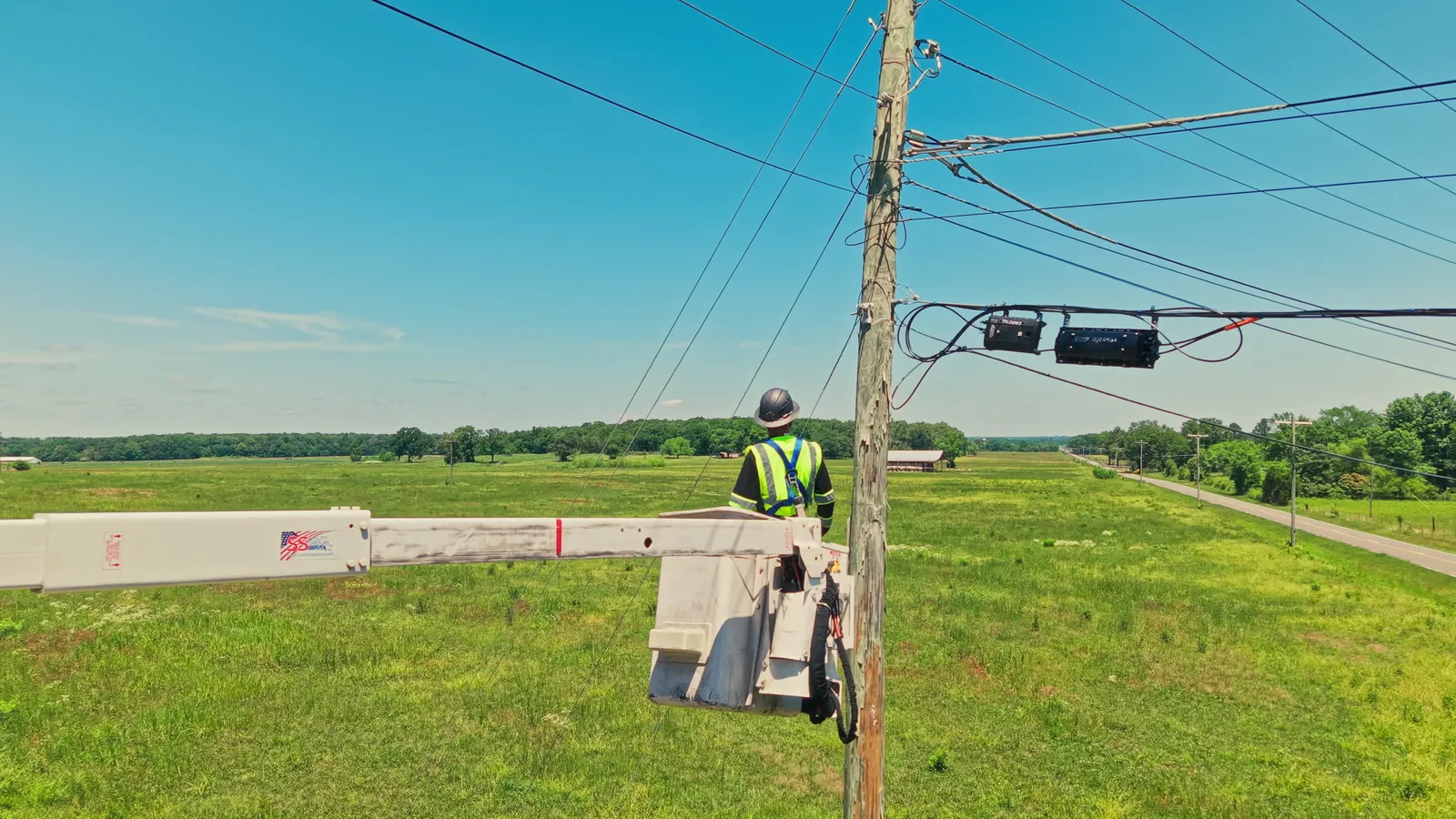 NextGen Fiber lineman in the bucket at a pole line with splice enclosures on strand